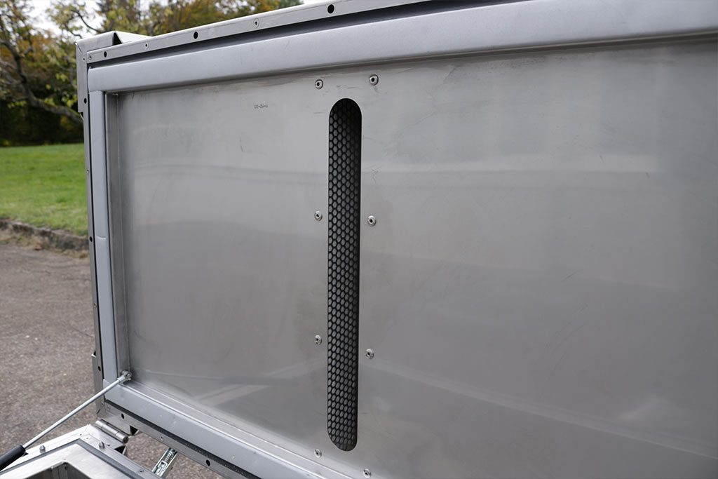 Metalplade med et sort ventilationsgitter med fine masker, omgivet af en sølvfarvet ramme.