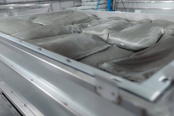 En grÄ, industriel rustfri stÄlbalje fyldt med uÄbnede sÊkke med grÄt pulver, med mange detaljer.