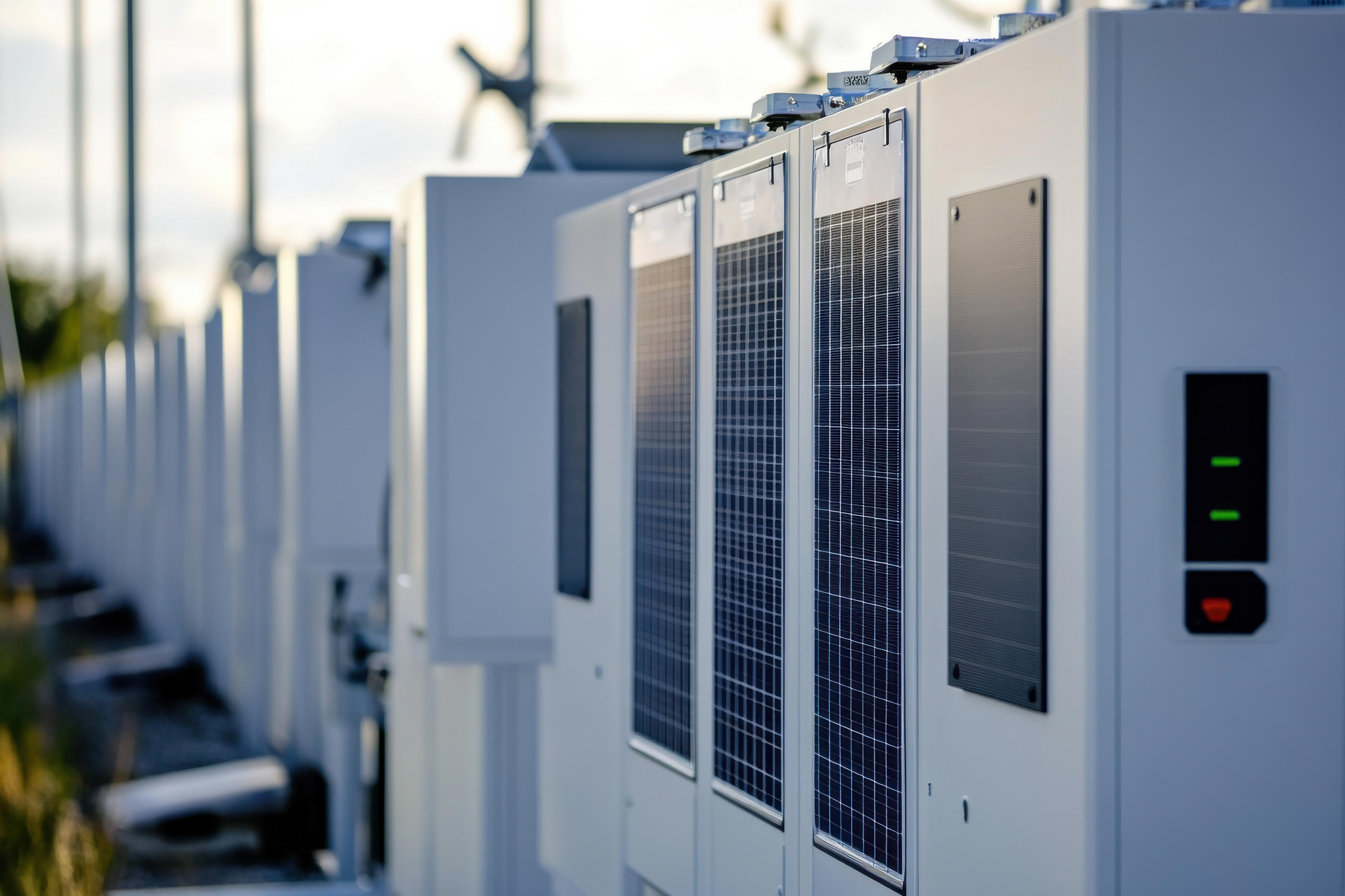En række hvide batterilagringsanlæg udendørs ved solnedgang; moderne energiinfrastruktur.